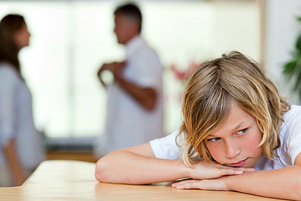 Sad looking boy with his fighting parents behind him