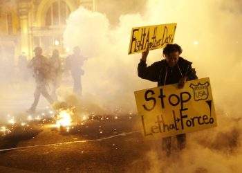 A woman runs for safety as police throw tear gas canisters while enforcing curfew, Tuesday, April 28, 2015, in Baltimore, a day after unrest that occurred following Freddie Gray's funeral. (AP Photo/Patrick Semansky)