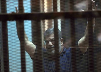 Ousted Egyptian President Mohammed Morsi raises his hands as he sits behind glass in a courtroom, in a converted lecture hall in the national police academy in an eastern Cairo suburb, Egypt, Saturday, May 16, 2015. An Egyptian court on Saturday sentenced ousted President Mohammed Morsi to death over his part in a mass prison break that took place during the 2011 uprising that toppled Hosni Mubarak. (AP Photo/Ahmed Omar)