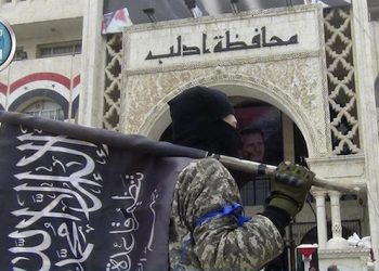 FILE - In this file photo posted on the Twitter page of Syria's al-Qaida-linked Nusra Front on Saturday, March 28, 2015, which is consistent with AP reporting, a fighter from Syria's al-Qaida-linked Nusra Front holds his group flag as he stands in front of the governor building in Idlib province, north Syria. In Syria, al-Qaida's Nusra Front is the most powerful fighting force outside the territories held by the Islamic State group. Last month, it worked with other rebel factions, including ones backed by Saudi Arabia, Turkey and Qatar, to capture the northwestern city of Idlib and territory in the south _ the biggest victories in several years over President Bashar Assad.  (Al-Nusra Front Twitter page via AP, File)