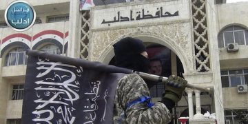 FILE - In this file photo posted on the Twitter page of Syria's al-Qaida-linked Nusra Front on Saturday, March 28, 2015, which is consistent with AP reporting, a fighter from Syria's al-Qaida-linked Nusra Front holds his group flag as he stands in front of the governor building in Idlib province, north Syria. In Syria, al-Qaida's Nusra Front is the most powerful fighting force outside the territories held by the Islamic State group. Last month, it worked with other rebel factions, including ones backed by Saudi Arabia, Turkey and Qatar, to capture the northwestern city of Idlib and territory in the south _ the biggest victories in several years over President Bashar Assad.  (Al-Nusra Front Twitter page via AP, File)