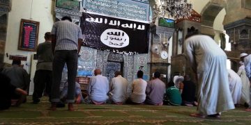 epa04307451 Worshipers pray at the Al-Noori Al-Kabeer mosque, next to flag used by the Islamic State (IS), in Mosul city, northern Iraq, 09 July 2014. Abu Bakr al-Baghdadi, the leader of the Sunni extremist group Islamic State appeared for the first time on 04 July at Al-Noori Al-Kabeer mosque in Mosul city, as he was purportedly delivering the noon prayer's sermon. Fighters of IS, an al-Qaeda splinter group, have in recent weeks seized large parts of northern and western Iraq, including Mosul, and made a swift advance to capture a string of towns stretching south towards Baghdad.  EPA/STR