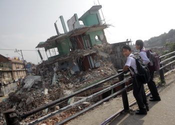 Nepalese students wait for their school bus in front of a collapsed house as thousands of schools across the districts worst hit by two major earthquakes in Nepal reopened Sunday, in Kathmandu, Nepal, Sunday, May 31, 2015. With most school buildings damaged or unsafe, the Education Ministry ordered that classes be held in temporary classrooms. According to a UNICEF statement, 32,000 classrooms were destroyed and 15,352 classrooms were damaged after the two major earthquakes in Nepal. (AP Photo/Niranjan Shrestha)