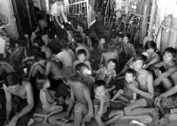 Vietnamese refugees rest as crewmen aboard the guided missile cruiser USS FOX (CG-33) give them something to drink.