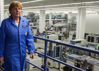 epa04634195 German Chancellor Angela Merkel wears a Siemens company smock during her visit to the Siemens electronics factory (EWA) in Amberg, Germany, 23 February 2015. Chancellor Merkel was given information about digitalization of the industry during her visit to Bavaria. The factory is considered to be the prime example of the Siemens 'digital factory' business field.  EPA/ARMIN†WEIGEL