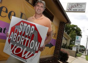 In this Friday, Aug. 23, 2013 photo, Troy Newman, head of the Wichita-based Operation Rescue holds an anti-abortion sign outside his headquarters housed in a closed abortion clinic in Wichita, United States. Australia's highest court ruled on Friday Oct. 2, 2015, that an American anti-abortion activist Troy Newman entered the country illegally and should be deported, amid concerns that he could incite violence against women and medical practitioners. (AP Photo/Charlie Riedel)