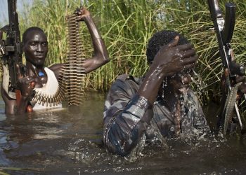 FILE - In this Saturday, Sept. 20, 2014 file photo, rebel soldiers patrol and protect civilians from the Nuer ethnic group as the civilians walk through flooded areas to reach a makeshift camp for the displaced situated in the United Nations Mission in South Sudan (UNMISS) base in the town of Bentiu, South Sudan. A long-awaited report by African Union investigators, released lated Tuesday, Oct. 27th, 2015 says mass graves have been discovered in South Sudan, cites horrific crimes against civilians including forced cannibalism, and disputes that there was a coup attempt by former Vice President Riek Machar in December 2013, finding that the conflict began with a skirmish between members of the presidential guard in the capital Juba. (AP Photo/Matthew Abbott, File)