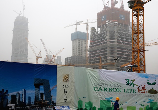 A worker sweeps near a billboard display showing a scene of Central Business District and a message encourage people on environment protection, as capital city skylines are shrouded with pollutant haze in Beijing, China, Monday, Nov. 9, 2015. Heading into this month's Paris meeting, the world's biggest source of climate-changing gases has yet to accept binding limits. But it has invested in solar, wind and hydro power to clean up its smog-choked cities and curb surging demand for imported oil and gas. That contributed last year to a surprise fall in coal consumption. (AP Photo/Andy Wong)