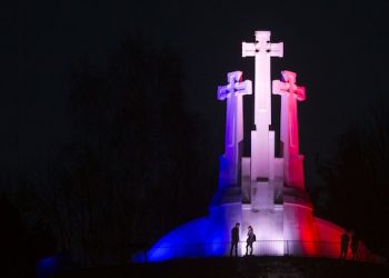 People walk near the Three Crosses in Vilnius, Lithuania, Sunday, Nov. 15, 2015, illuminated by the colors of the French national flag in solidarity with France after the attacks in Paris. (AP Photo/Mindaugas Kulbis)