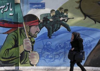 An Iranian woman walks past a mural depicting Iranian armed forces in the battlefield, at Palestine Sq. in Tehran, Iran, Saturday, Jan. 16, 2016. The end of Western sanctions against Iran loomed Saturday as Iran's foreign minister suggested the U.N. atomic agency is close to certifying that his country has met all commitments under its landmark nuclear deal with six world powers. (AP Photo/Vahid Salemi)