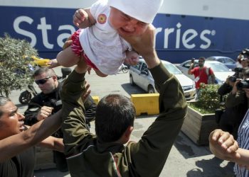 A migrant man holds a baby over his shoulders during tension with port police officers at the Athens port of Piraeus, Wednesday, April 6, 2016. The man grabbed the  few-months-old baby and threatened to throw her at police, Greek media reported. Another man later took the child from his hands and handed her back to her mother. Dozens of migrants and refugees have been staging a sit-down protest in Greece's main port of Piraeus, where thousands have been camping out for weeks, after reports that authorities would try to move the people there into organised camps. (Yiorgos Baboukos/InTime News via AP)    GREECE OUT
