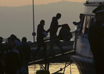 epa05243045 A migrant is escorted by a Frontex officer into a ferry in the port of Mytilene, Lesvos island, Greece, 04 April 2016. Some 160 migrants, from Pakistan, Bangladesh and Morroco, who refused to apply for asylum, have been deported on 04 April early morning to Turkey, after the agreement between European Union (EU) and Turkey on the refugees crisis.  EPA/ORESTIS PANAGIOTOU