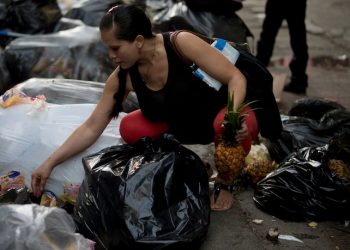 This June 2, 2016 photo shows a pregnant woman who did not want to be named, holding a pineapple in one hand as she continues to pick through garbage bags outside a supermarket in downtown Caracas, Venezuela. Unemployed people converge every dusk at the trash heap to pick through rotten fruit and vegetables tossed out by nearby shops. (AP Photo/Fernando Llano)