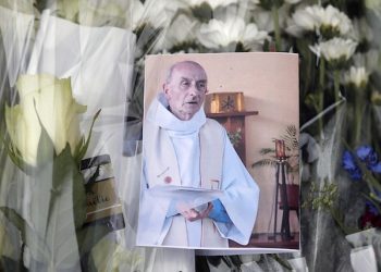 A picture of late Father Jacques Hamel is placed on flowers at the makeshift memorial in front of the city hall closed to the church where an hostage taking left a priest dead the day before in Saint-Etienne-du-Rouvray, Normandy, France, Wednesday, July 27, 2016. The Islamic State group crossed a new threshold Tuesday in its war against the West, as two of its followers targeted a church in Normandy, slitting the throat of an elderly priest celebrating Mass and using hostages as human shields before being shot by police. (AP Photo/Francois Mori)