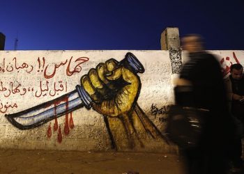 epa05117130 Palestinians walk in front of a graffiti depicting a hand holding a knife, in support of the third Palestinian 'intifada' or uprising, in the streets of Gaza City, 21 January 2016.  EPA/MOHAMMED SABER