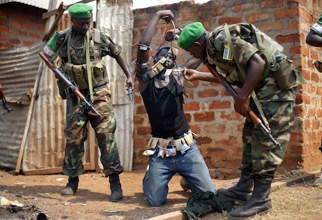 FILE- In this Wednesday Jan. 22, 2014 photo, Rwandan African Union peacekeepers remove the lucky charms from a suspected Anti-Balaka Christian man who was found with a rifle and a grenade following looting in the Muslim market of the PK13 district of Bangui, Central African Republic. A sweeping United Nations report has identified hundreds of human rights violations in Central African Republic that may amount to war crimes. The Tuesday may 30, 2017, report comes amid growing fears that the country terrorized by multiple armed groups is once again slipping into the sectarian bloodshed that left thousands dead between late 2013 and 2015. (AP Photo/Jerome Delay-File)