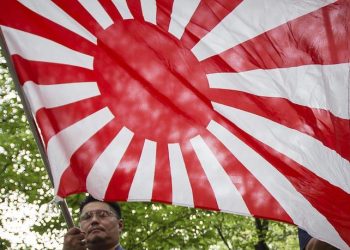 epa05486232 A Japanese right-wing group member holding a Rising Sun Flag offers a moment of silence for the war dead on the grounds of the Yasukuni Shrine in Tokyo, Japan, 15 August 2016. Japan marks the 71st anniversary of the end of the World War II on 15 August. About 3.1 million Japanese soldiers and people were killed during the war, almost 2.5 million of whom are enshrined at Yasukuni, including convicted WWII war criminals.  EPA/CHRISTOPHER JUE