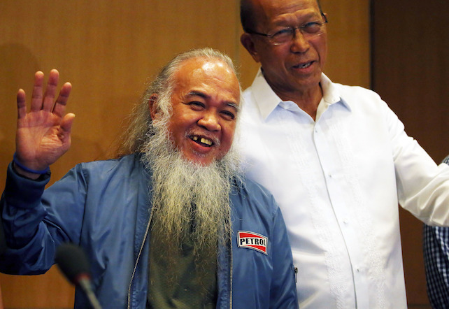 Rescued Roman Catholic priest Father Teresito Soganub, waves as he is presented to the media in a news conference Monday, Sept. 18, 2017 at Camp Aguinaldo in suburban Quezon city northeast of Manila, Philippines. Philippine troops have rescued Father Soganub and another civilian who were among dozens of people abducted in May when hundreds of militants aligned with the Islamic State group laid siege on southern Marawi city, officials said. At right is Defense chief Delfin Lorenzana. (AP Photo/Bullit Marquez)