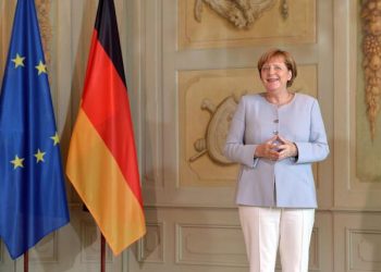epa05420916 A smiling German Chancellor Angela Merkel stands next to a European Union (EU) and a German national flag as she waits for the arrival of the guests during a reception of the Diplomatic Corps at the German government's guesthouse in Meseberg, Germany, 11 July 2016.  EPA/MAURIZIO GAMBARINI