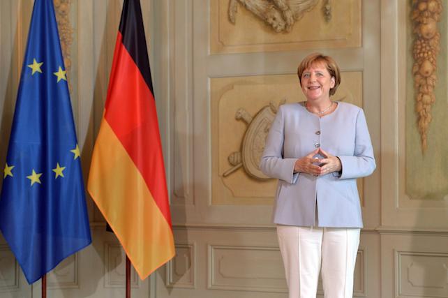 epa05420916 A smiling German Chancellor Angela Merkel stands next to a European Union (EU) and a German national flag as she waits for the arrival of the guests during a reception of the Diplomatic Corps at the German government's guesthouse in Meseberg, Germany, 11 July 2016.  EPA/MAURIZIO GAMBARINI