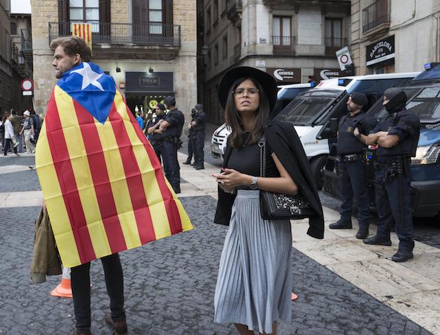 epa06238031 A couple with a Catalonian flag near Spanish police in the Placa Sant Jaume, or the Town Hall Square, in Barcelona, Spain 01 October 2017. Catalonia is holding an independence referendum which has been declared illegal by the Spanish Constitutional Court.  EPA/JIM HOLLANDER