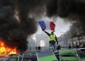 A demonstrator waves the French flag onto a burning barricade on the Champs-Elysees avenue with the Arc de Triomphe in background, during a demonstration against the rise of fuel taxes, Saturday, Nov. 24, 2018 in Paris. French police fired tear gas and water cannons to disperse demonstrators in Paris Saturday, as thousands gathered in the capital and staged road blockades across the nation to vent anger against rising fuel taxes and Emmanuel Macron's presidency.(ANSA/AP Photo/Michel Euler) [CopyrightNotice: Copyright 2018 The Associated Press. All rights reserved.]