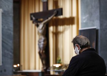 Un uomo con mascherina contro il coronavirus in preghiera in una chiesa di Roma