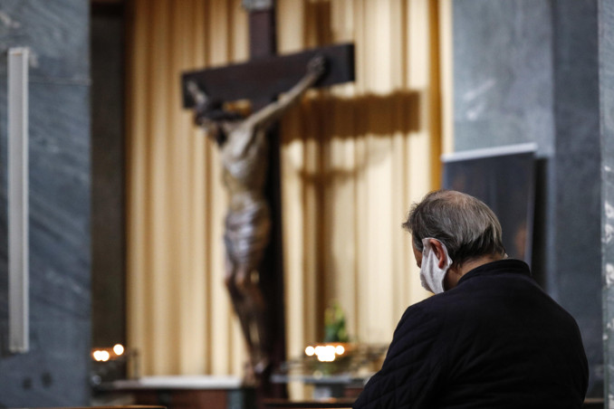 Un uomo con mascherina contro il coronavirus in preghiera in una chiesa di Roma