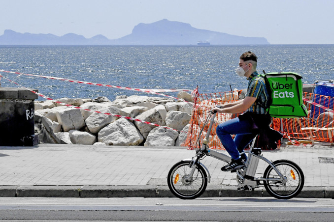 Rider effettua consegne in bicicletta sul lungomare di Napoli