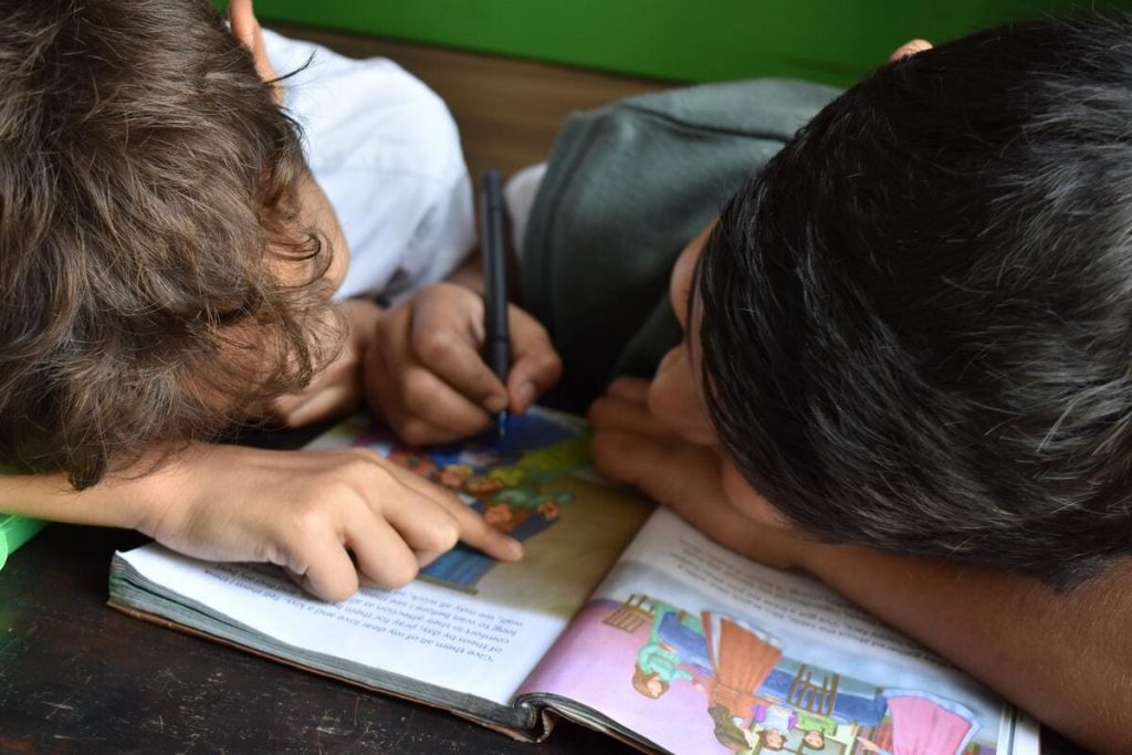 scuola, due studenti colorano un quaderno seduti al banco