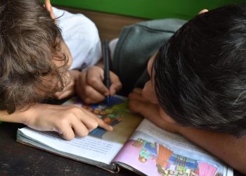 scuola, due studenti colorano un quaderno seduti al banco