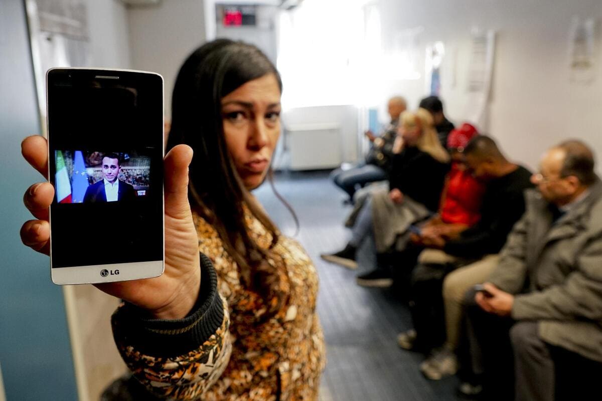 Una donna in fila per fare domanda per il reddito di cittadinanza mostra un telefonino con la foto del ministro Luigi Di Maio