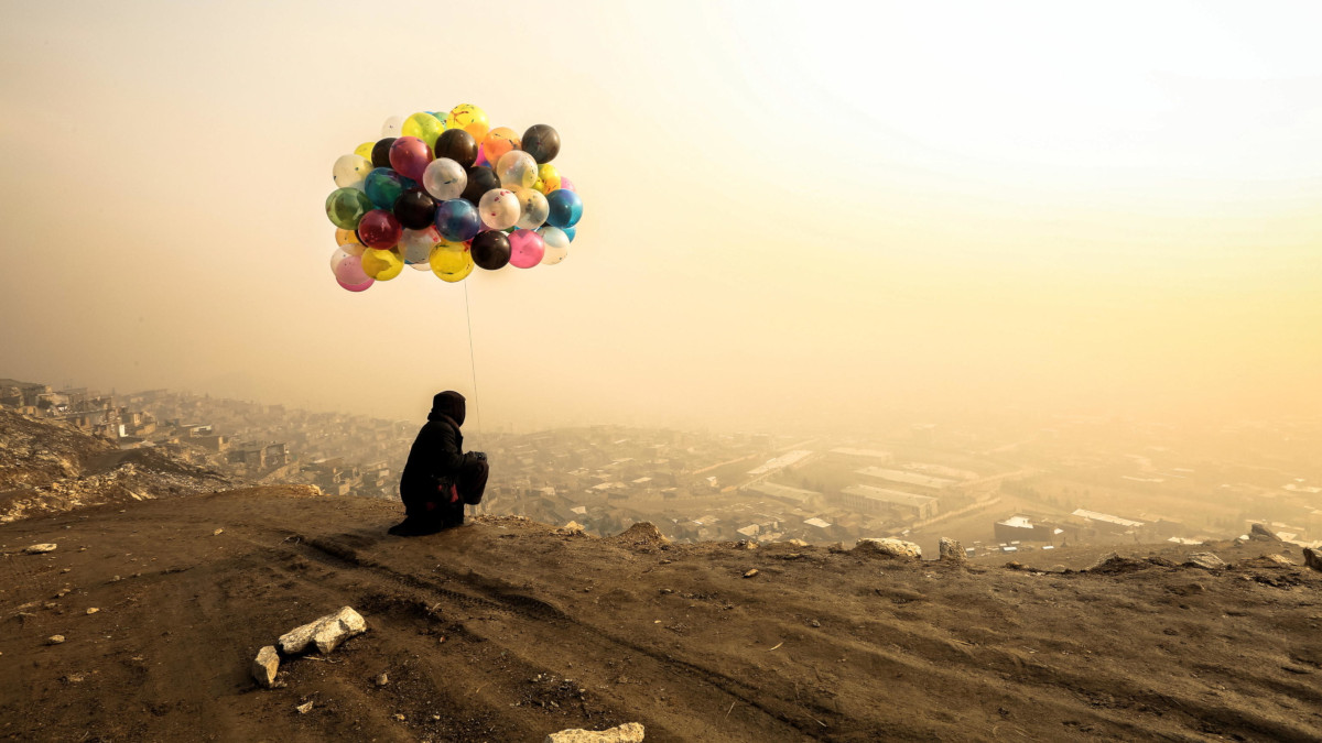 Venditrice di palloncini davanti a Kabul avvolta nella nebbia