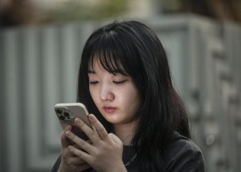 Una ragazza cinese guarda il suo smartphone nelle vie di Shanghai (foto Ansa)