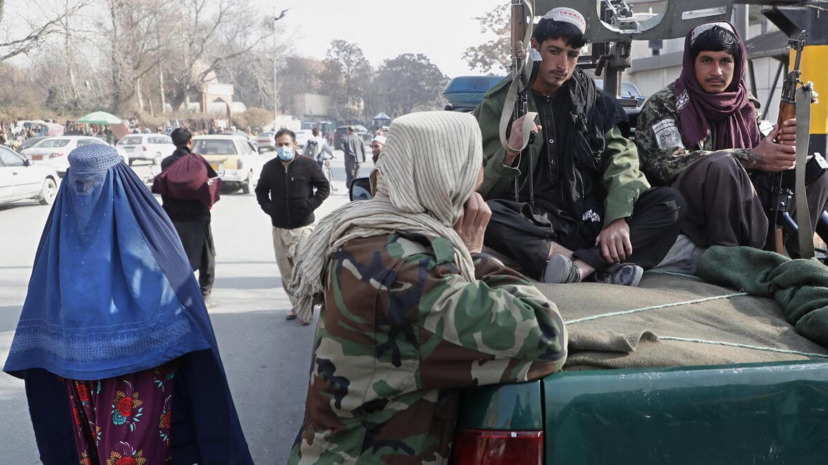 Una donna con il burqa passa di fianco a un gruppo di talebani in Afghanistan
