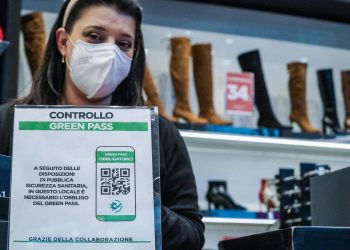 Una negoziante a Torino mostra il cartello del controllo del green pass