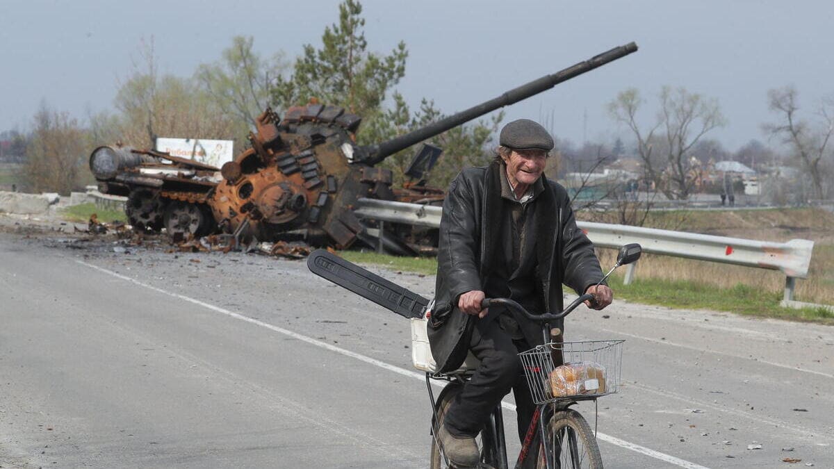 Un uomo in bicicletta oltrepassa un carro armato russo distrutto vicino a Kiev, in Ucraina