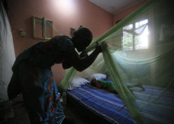 Una donna in Africa installa una zanzariera sul letto del figlio per proteggerlo dalla malaria