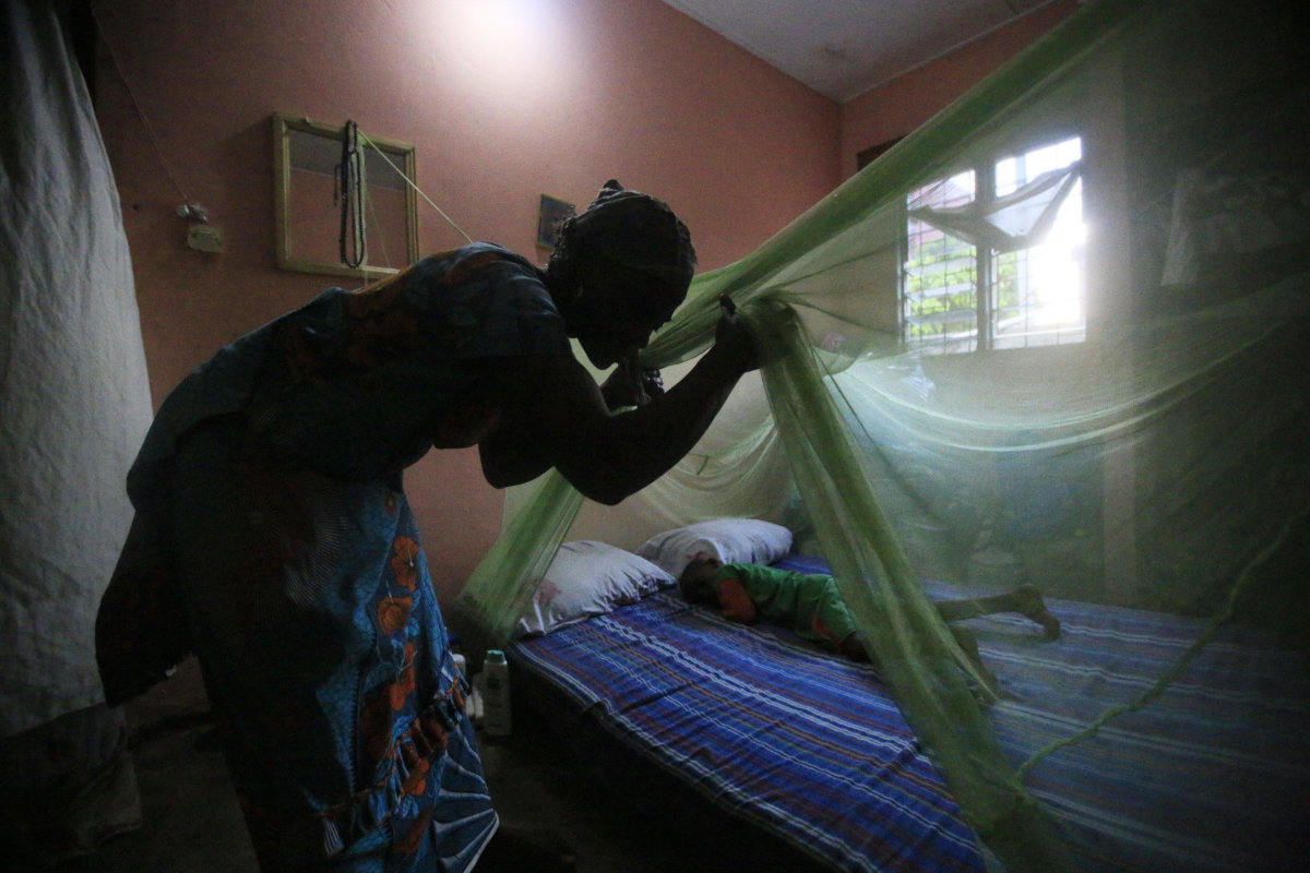 Una donna in Africa installa una zanzariera sul letto del figlio per proteggerlo dalla malaria