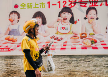 Un corriere davanti a un manifesto pubblicitario di prodotti alimentari a Pechino