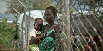 Una donna con un figlio in braccio in un campo per sfollati interni prevalentemente di etnia dinka a Mingkaman, Sud Sudan, 2014