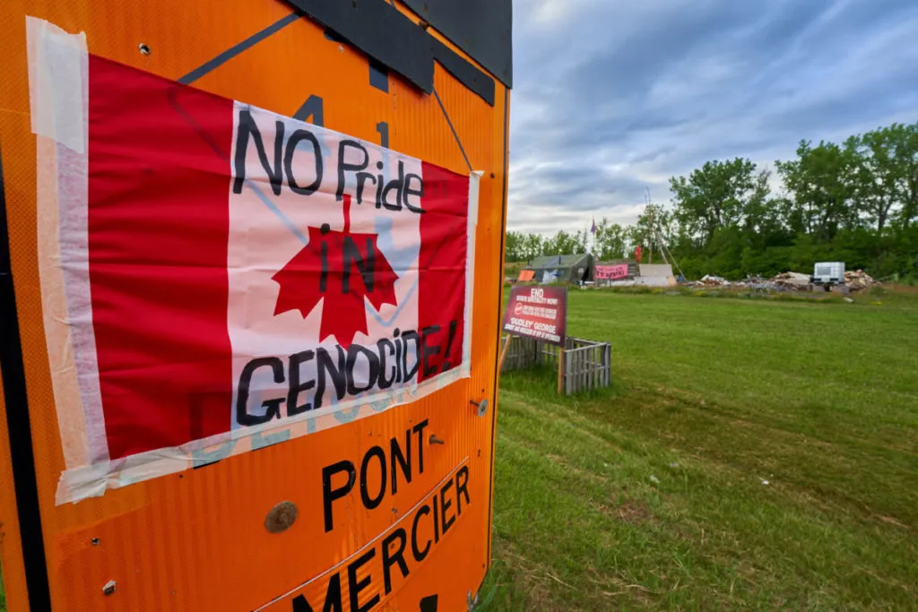 Bandiera canadese rovesciata con lo slogan &ldquo;Nessun orgoglio nel genocidio&rdquo; esposta in protesta dopo il ritrovamento della presunta fossa comune della scuola residenziale di Kamloops, riserva Kahnawake, Canada, 2 luglio 2021