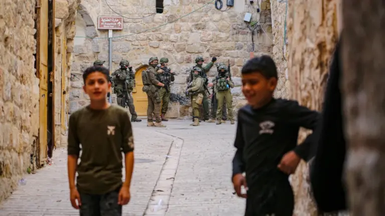 Due ragazzini palestinesi nella città vecchia di Hebron; alle loro spalle, soldati israeliani, 31 maggio 2025 (foto Ansa)