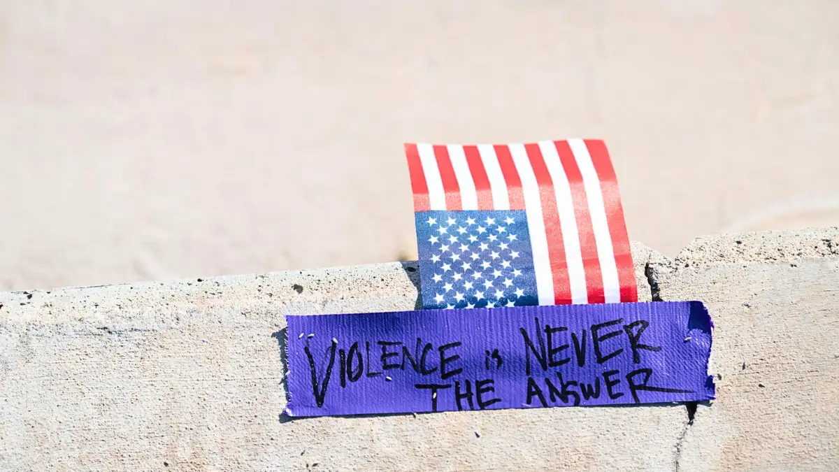La scritta “la violenza non è mai la risposta” su un nastro adesivo che tiene ferma una bandiera americana sul luogo in cui Charlie Kirk è stato ucciso (foto Ansa)