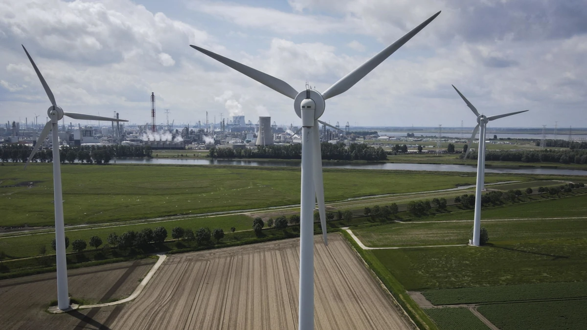 Le pale del parco eolico di Berendrecht, al confine tra Belgio e Olanda. Sullo Sfondo l’impianto industriale Basf di Antwerp e la centrale nucleare di Doel (foto Ansa)