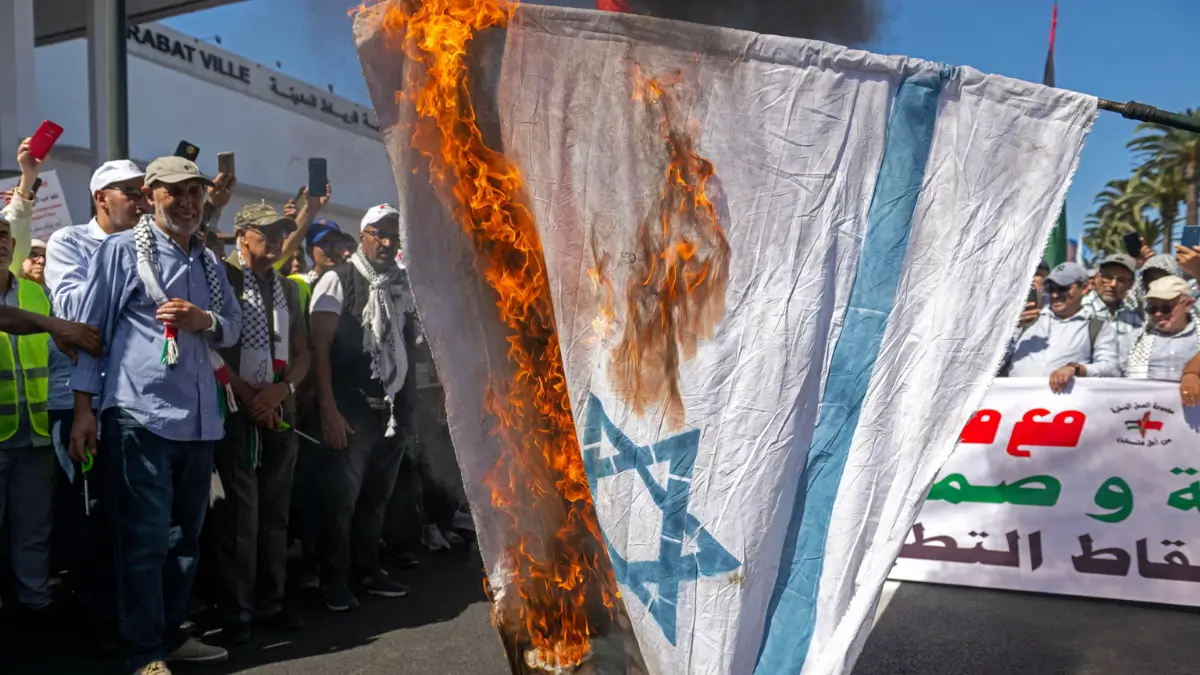 Una bandiera israeliana data alle fiamme da alcuni manifestanti pro Gaza in Marocco piano Trump