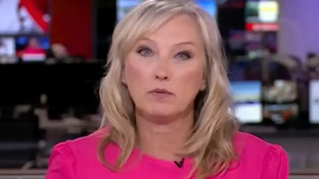 La giornalista di Bbc News Martine Croxall con capelli biondi e camicetta rosa shocking guarda direttamente verso la telecamera con un'espressione seria. Si trova in uno studio televisivo moderno con numerosi schermi e monitor in background che mostrano grafiche e altri contenut