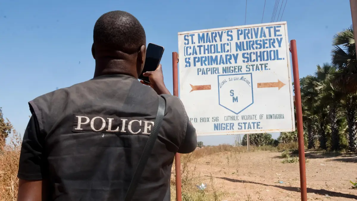 Un uomo delle forze di polizia in Nigeria di fronte al cartello della St. Mary's School di Papiri in cui sono stati rapiti oltre 300 studenti cristiani cattolici