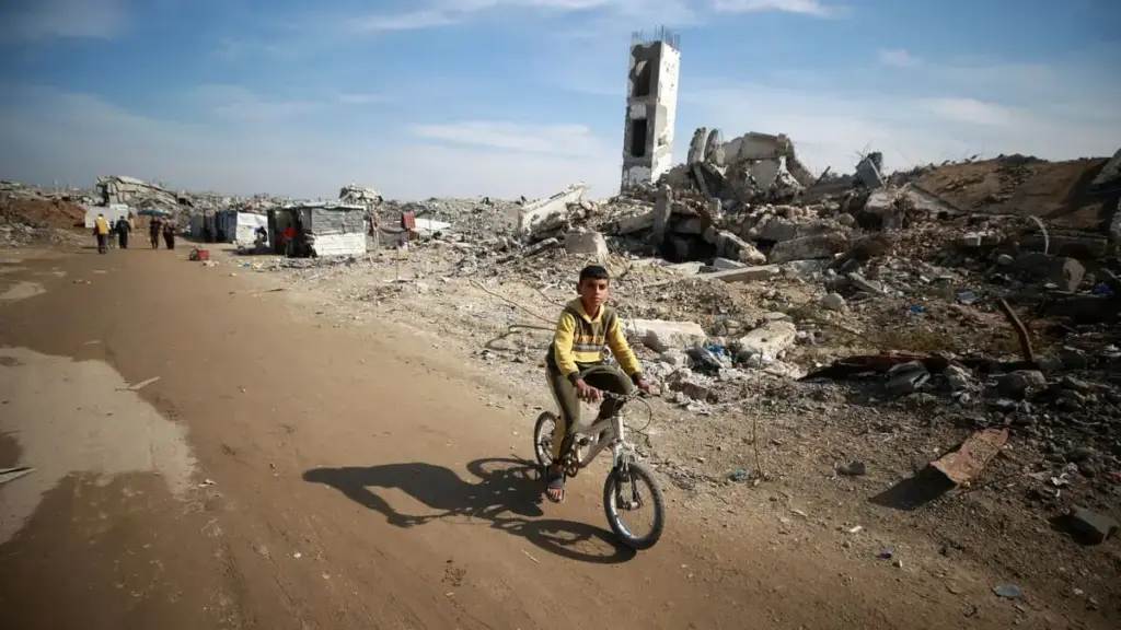 Un bambino va in bicicletta a Gaza di fianco alle macerie dei palazzi distrutti
