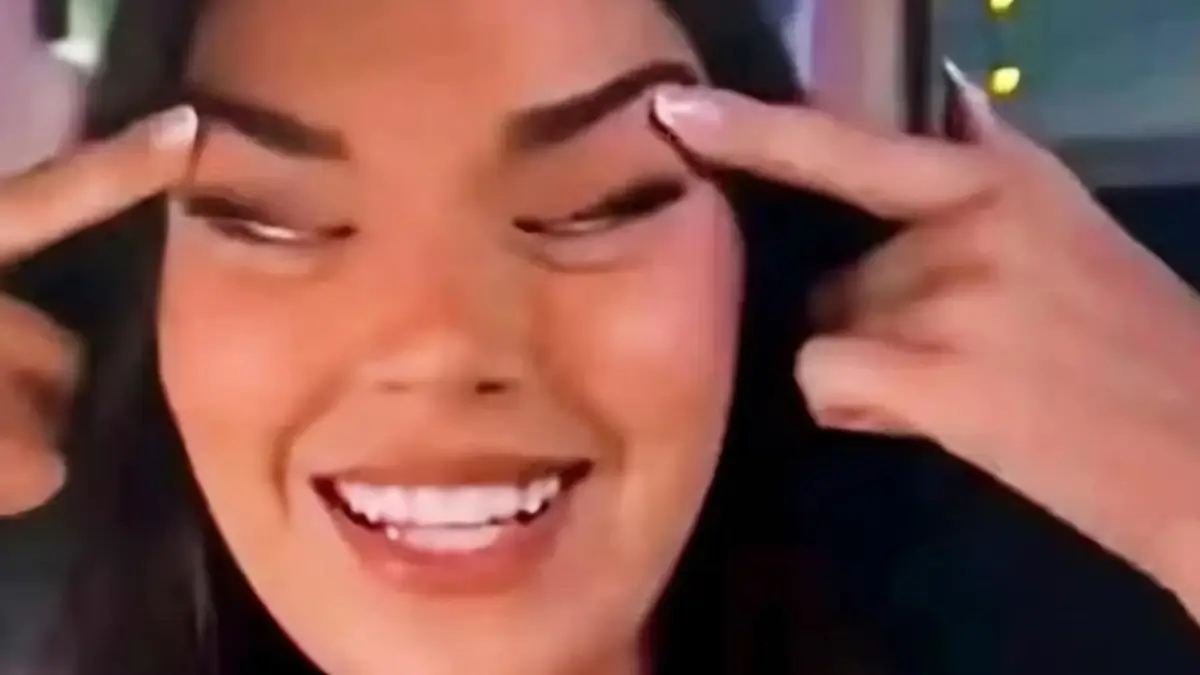Primo piano di Sarah Dzafce, Miss Finlandia 2025, che sorride sollevando con le dita gli angoli esterni delle sopracciglia e degli occhi verso l'alto